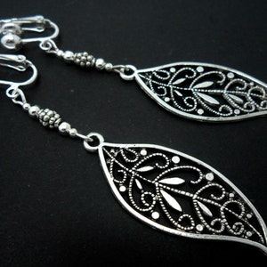 May include: Silver clip-on earrings featuring a leaf design. The leaves are filigree and have a delicate, intricate pattern.