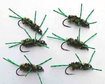 May include: Six fishing flies featuring a fuzzy black and olive green chenille body, a metallic bead head, and multiple protruding green rubber legs with black stripes. Each fly is attached to a curved metal hook, designed for fly fishing.