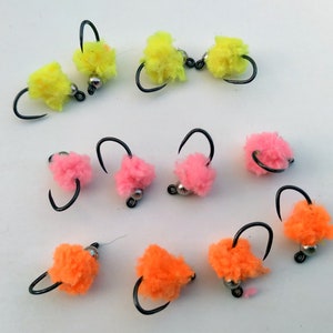 May include: Assortment of colorful fly fishing lures with fluffy yarn bodies in yellow, pink, and orange.