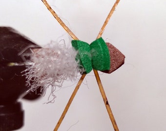May include: A fly tying material kit with two brown sticks, a white fluffy material, and a green and brown bead.