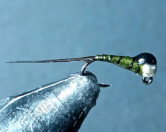May include: A green and silver fly fishing lure with a black bead. The lure is tied on a hook and is ready to be cast.