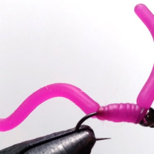 May include: A pink rubber worm fly fishing lure with a silver bead.