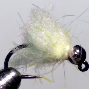 May include: Close-up of a handmade fishing fly. The fly features a silver bead head, a black hook, and a body made of white, fluffy material with iridescent accents. The fly is designed for attracting fish.