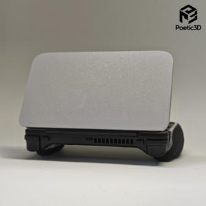 以下が含まれることがあります： マットシルバーのトップカバーとブラックのベースを備えた携帯型ゲーム機。デバイスには、水平方向の通気グリル、小さなポート、側面に統合されたコントローラーグリップが含まれています。右上にPoetic3Dのロゴが表示されています。
