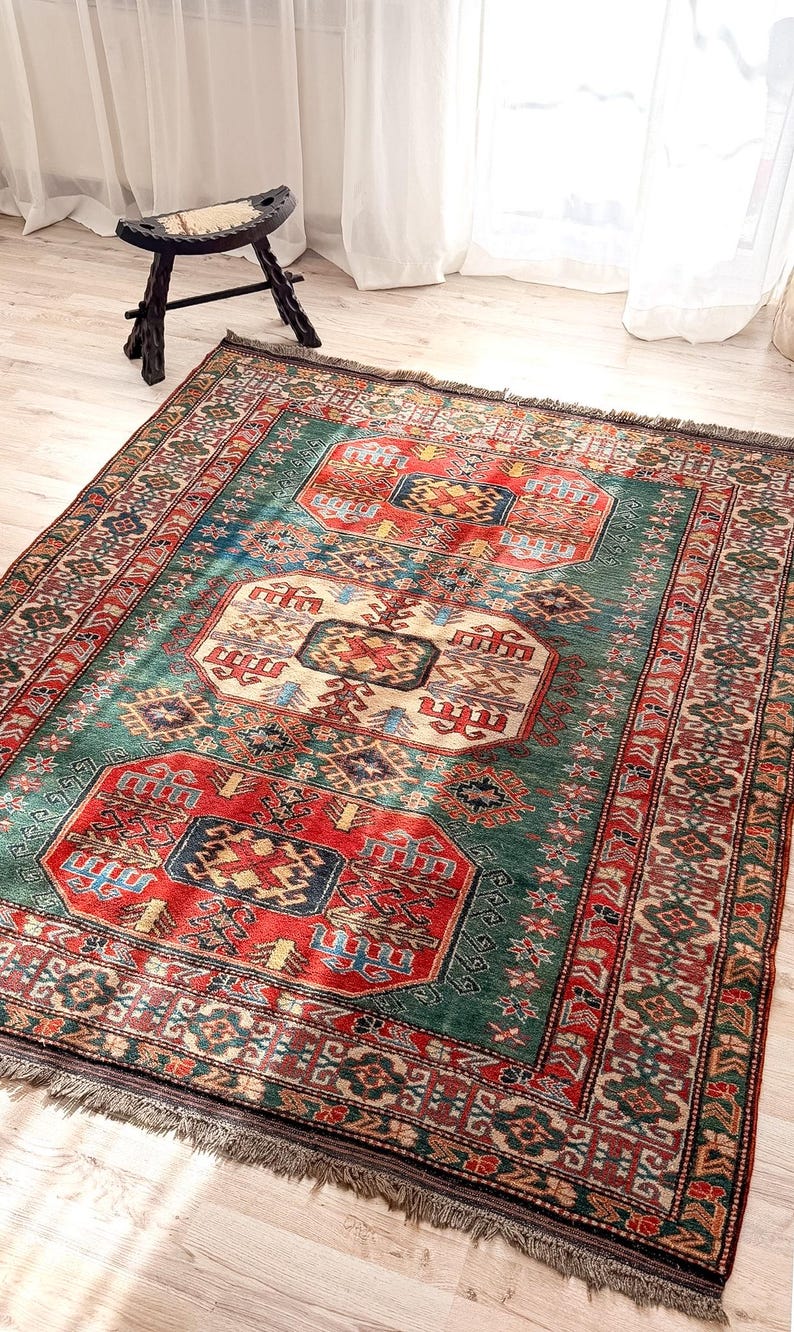 Puede incluir: Una alfombra rectangular con un complejo patr&oacute;n geom&eacute;trico en tonos rojo intenso, verde bosque, azul marino y crema. La alfombra tiene un borde decorativo ancho con motivos intrincados y flecos cortos en los extremos de la tela.