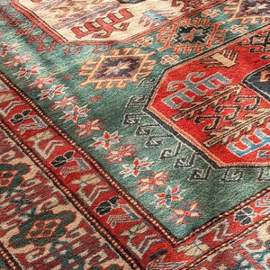 Puede incluir: Una alfombra rectangular con un patr&oacute;n geom&eacute;trico complejo en tonos rojo intenso, verde bosque, crema y azul marino. El dise&ntilde;o incluye medallones repetitivos, bordes intrincados y motivos florales estilizados en toda la superficie.
