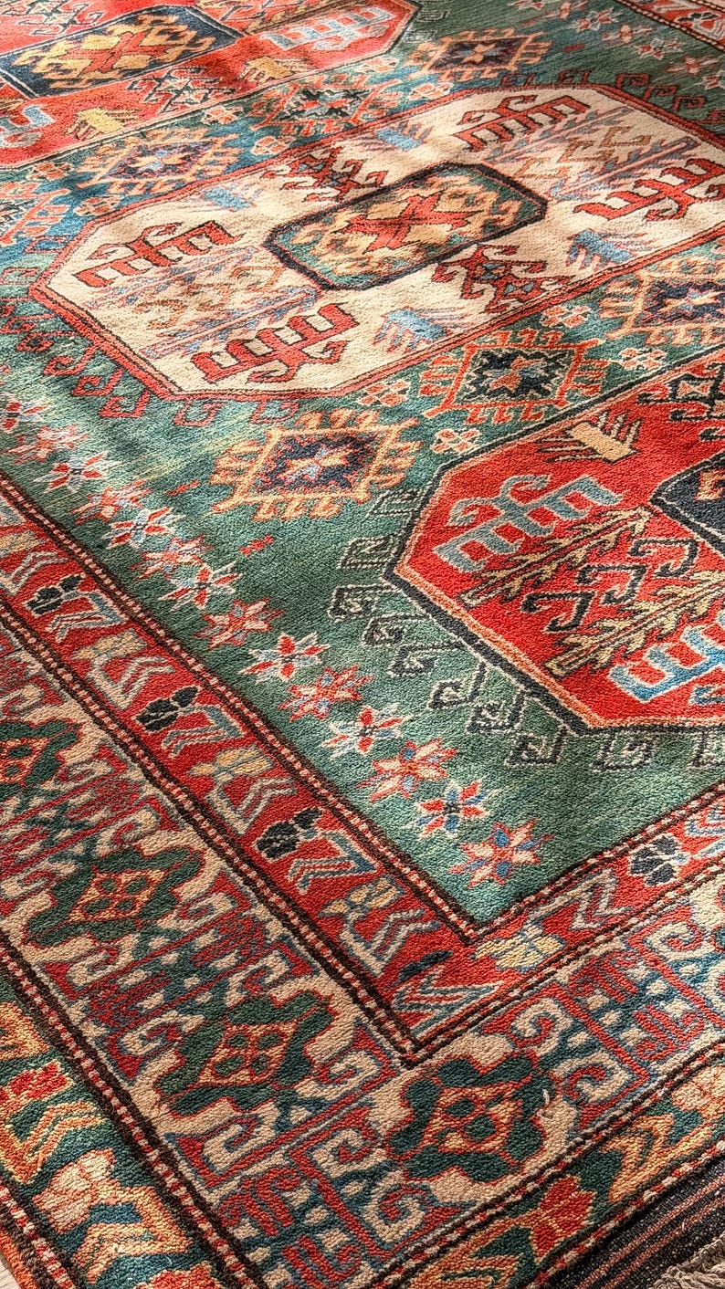 Puede incluir: Una alfombra rectangular con un patr&oacute;n geom&eacute;trico complejo en tonos rojo intenso, verde bosque, crema y azul marino. El dise&ntilde;o incluye medallones repetitivos, bordes intrincados y motivos florales estilizados en toda la superficie.