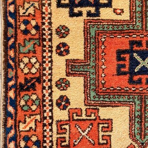 K&ouml;nnte beinhalten: Ein gewebter Teppich mit cremefarbenem Feld und geometrischen Mustern in Orange, Marineblau und Salbeigr&uuml;n. Die Bord&uuml;re zeigt ein sich wiederholendes Blumenmotiv in Orange und Blau, eingerahmt von einem dunkelblauen Rand mit gekn&uuml;pfter Struktur.