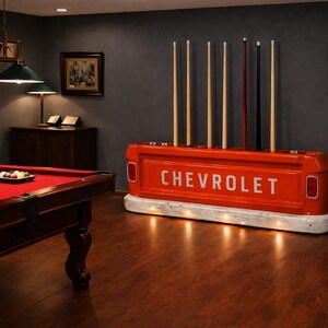 Op de afbeelding: Een rode pooltafel met een rood vilt oppervlak en een set biljartballen. Een op maat gemaakte keurrek van een vintage Chevrolet-truckbed staat op de achtergrond. De rek is oranje met het woord "CHEVROLET" in het wit.