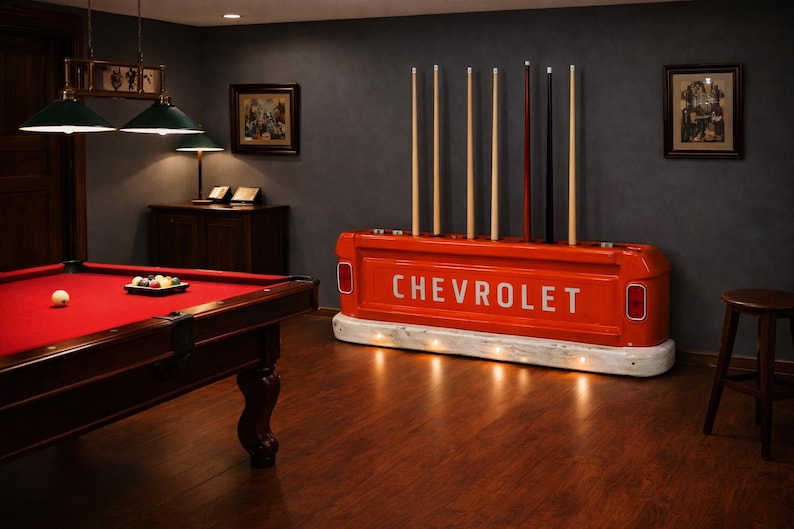 Op de afbeelding: Een rode pooltafel met een rood vilt oppervlak en een set biljartballen. Een op maat gemaakte keurrek van een vintage Chevrolet-truckbed staat op de achtergrond. De rek is oranje met het woord "CHEVROLET" in het wit.