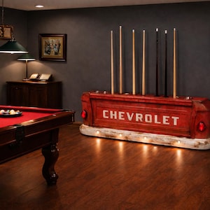 Op de afbeelding: Een rode Chevrolet-vrachtwagenbak hergebruikt als keurrek, met het woord "CHEVROLET" in het wit. Het rek bevat verschillende keuen. Een rode pooltafel met een rood vilt is op de voorgrond.