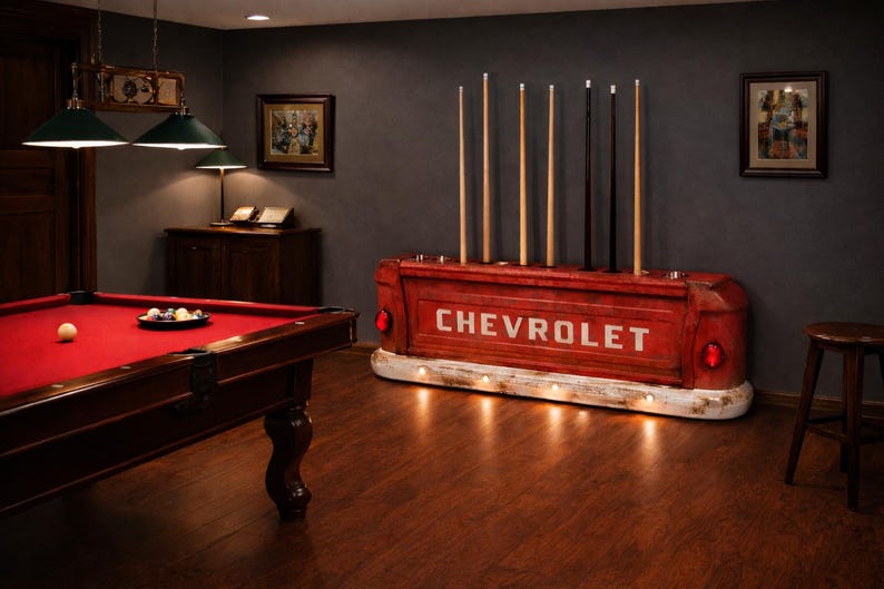 Op de afbeelding: Een rode Chevrolet-vrachtwagenbak hergebruikt als keurrek, met het woord "CHEVROLET" in het wit. Het rek bevat verschillende keuen. Een rode pooltafel met een rood vilt is op de voorgrond.