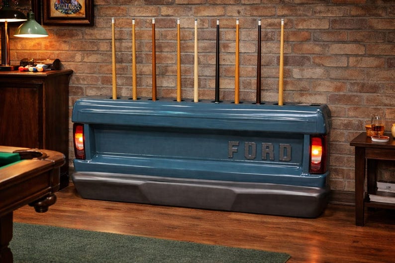Op de afbeelding: Een blauwe Ford-vrachtwagenbak omgebouwd tot een keurek. De houder bevat verschillende keuen in verschillende kleuren. Het Ford-logo is zichtbaar. De houder heeft werkende achterlichten. De achtergrond is een bakstenen muur.