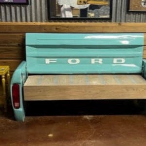 May include: A turquoise blue bench made from the back of a Ford truck. The bench has a wooden seat and the Ford logo is visible on the back. Two small yellow side tables are on either side of the bench.