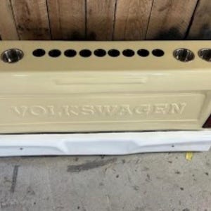 Op de afbeelding: Beige op maat gemaakte achterklep met het woord "VOLKSWAGEN" in reli&euml;f. Het heeft meerdere bekerhouders en een witte bumper eronder. Rode achterlichten zijn zichtbaar.