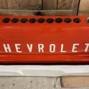 Op de afbeelding: Een oranje Chevrolet achterklepbar met het woord "CHEVROLET" in het wit. Het heeft verschillende bekerhouders en een witte bumper. De bar is ontworpen om op de achterkant van een klassieke pick-up truck te lijken.