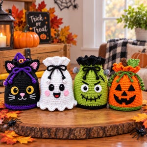 May include: Four crocheted drawstring bags featuring Halloween designs: a black cat with a purple witch hat, a white ghost with pink cheeks, a green monster with bolts, and an orange jack-o'-lantern with a green stem and leaves.