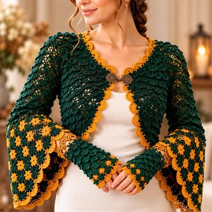 May include: A dark green crochet bolero with long flared sleeves featuring yellow floral patterns at the cuffs and edges. The garment has a scalloped yellow trim and is fastened at the center with an ornate, metallic bronze-toned clasp.