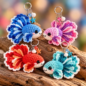 May include: Four crocheted betta fish keychains in blue, pink, red-orange, and teal. Each fish features a round body, large ruffled fins, and black bead eyes. Silver key rings are attached, adorned with small charms including a seashell and starfish.