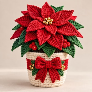 May include: A crocheted poinsettia plant with vibrant red petals and dark green leaves, featuring a center of small gold beads. The plant sits in a cream-colored pot with a red horizontal stripe, decorated with a large red crocheted bow and gold beads.