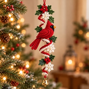 May include: A crocheted hanging ornament featuring a bright red cardinal bird perched on a spiral of red and white yarn, accented with green holly leaves, red berries, white snowflakes, and a small gold-colored metal bell at the bottom.