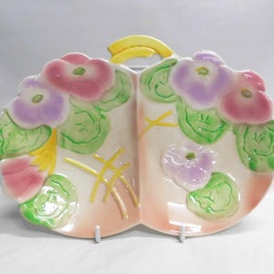 May include: A divided serving dish with a yellow handle, featuring pink and purple floral designs with green leaves. The dish has a light peach and white color scheme, with yellow accents.
