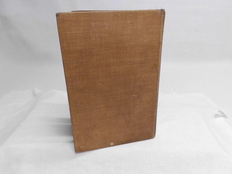 May include: A rectangular, brown, vintage book with a textured cover. The book is standing upright, with the spine facing the viewer. The cover has a slightly worn appearance, suggesting age and use. The book is set against a white background.