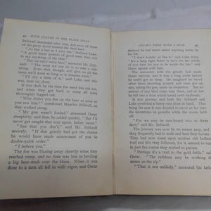 May include: Open book with text on aged paper. The left page has the title "WITH CESTER IN THE BLACK HILLS". The right page has the title "DICAR'S FIGHT WITH A BEAR".