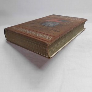 May include: A vintage book with a brown cover featuring an illustration and the title "The Motor Boys". The book's spine and pages are visible, with the author's name printed on the cover. The book is set against a white background.