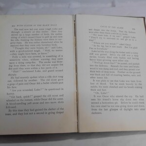 May include: Open book with text on both pages. The pages are yellowed with age, and the text is in black. The book is open to a chapter titled "With Custer in the Black Hills" and "Cause of the Alarm."