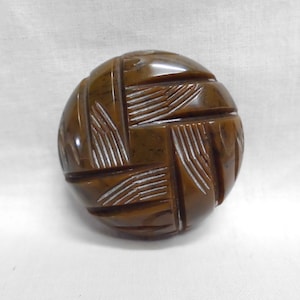 May include: A round, brown button with a carved geometric design. The button features a series of intersecting lines and a glossy finish. This decorative button is suitable for sewing projects and crafts.