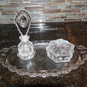 May include: A white ceramic mug with a black handle and the text "But First, Coffee" in a bold, black font. The mug is set against a blurred background, suggesting a cozy setting.