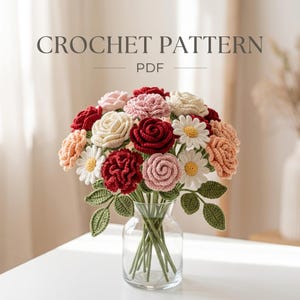 May include: A crochet pattern PDF featuring a bouquet of handmade yarn flowers in a clear glass vase. The arrangement includes red, pink, cream, and white roses and daisies with green crocheted leaves on long stems, displayed on a white surface.