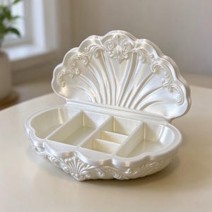 May include: A pearlescent white jewelry box shaped like an open seashell. The interior features four distinct compartments for storage, while the exterior lid and base are decorated with intricate, raised scrollwork and fan-like patterns.