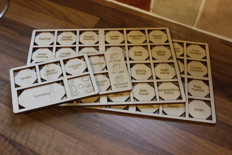 May include: Wooden game pieces with hexagonal shapes and various labels, including "Gazebo", "Dwelling", "Stone Collector", "Robbers' Lair", "Springs", "On River", "On Lake", "Milking Parlor", "State Parlor", "Guest Room", "Office Room", "Food Chamber", "Fodder Chamber", "Beer Parlor", "Blacksmithing Parlor", "Ruby Supplier", "Quarry", and "Seam".