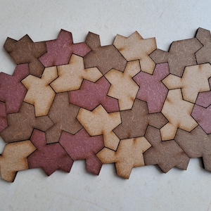 Könnte beinhalten: Ein geometrisches Puzzle aus Holz mit braunen und rosafarbenen Teilen. Die Teile sind sternförmig und fügen sich zu einem größeren Muster zusammen.