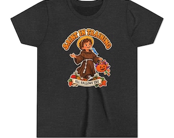 May include: A dark heather grey t-shirt featuring a graphic of a child dressed as a monk with a halo, holding a jack-o'-lantern bucket filled with sweets. The text reads SAINT IN TRAINING and ALL HALLOWS' EVE, surrounded by autumn leaves.