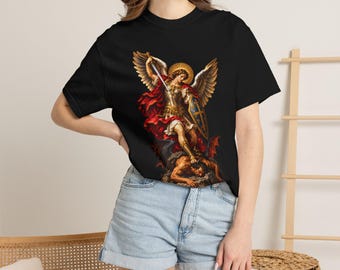 May include: A black short-sleeve t-shirt featuring a detailed graphic print of Saint Michael the Archangel in golden armor with wings, holding a sword and shield while standing over a fallen figure, rendered in vibrant red, gold, and brown tones.