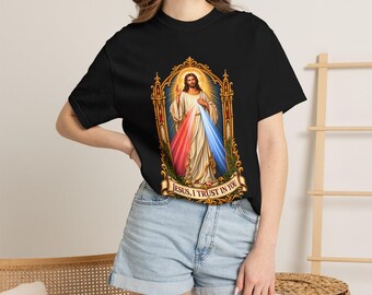 Può includere: Una t-shirt nera a maniche corte con una grafica centrale di Gesù Cristo all'interno di una cornice dorata decorata. La figura indossa vesti bianche con raggi rossi e blu che emanano dal petto. Sotto l'immagine, un cartiglio recita: JESUS, I TRUST IN YOU.