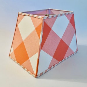 May include: A square lampshade with a pink and white gingham pattern. The lampshade has a white trim with a pink and white stripe pattern.