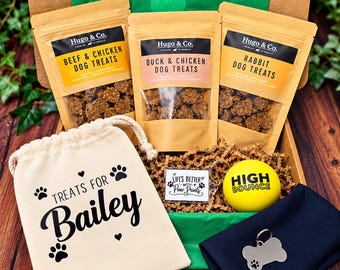 Può includere: Una scatola regalo in cartone contenente tre buste di premi per cani Hugo & Co. ai gusti manzo e pollo, anatra e pollo, e coniglio. Include un sacchetto color crema con la scritta Treats for Bailey, una pallina gialla e una medaglietta a osso.