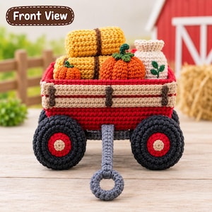 Könnte beinhalten: Ein gehäkelter roter Wagen mit schwarzen Rädern und einem grauen Griff, beladen mit zwei gelben Heuballen, zwei orangefarbenen Kürbissen und einem beigen Sack mit grünem Blattmotiv. Der Wagen hat hellbraune Holzlatten und ein Front-Etikett.