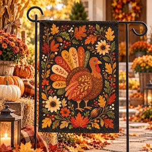 May include: A rectangular garden flag featuring a central turkey illustration surrounded by a decorative border of autumn leaves, sunflowers, and red berries on a black background, suspended from a black metal garden flag stand.