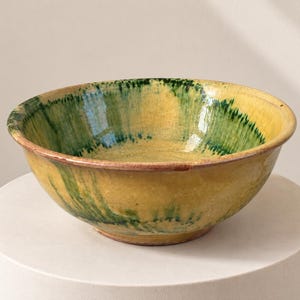 Peut inclure: Un bol en céramique rond présentant une glaçure jaune brillante avec des stries verticales de pigment vert foncé. Le bol possède un bord large et ouvert ainsi qu'une finition de surface lisse et réfléchissante, avec un motif coloré appliqué.