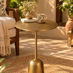 May include: A round gold side table with a textured, hammered metal surface on the tabletop and the base. The table features a slender central pedestal connecting the circular top to the dome-shaped base, creating a metallic accent piece.