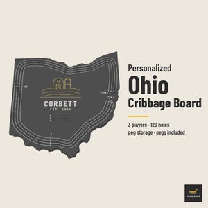 May include: A dark gray Ohio-shaped cribbage board featuring a white line graphic of a barn and silo, the text CORBETT EST. 2014, and a 120-hole track for 3 players. The text reads Personalized Ohio Cribbage Board, 3 players, 120 holes, peg storage, pegs included.