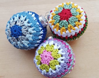May include: Three crocheted Christmas ornaments in blue, purple, and green with white and yellow accents. Each ornament features a different colored flower in the center.