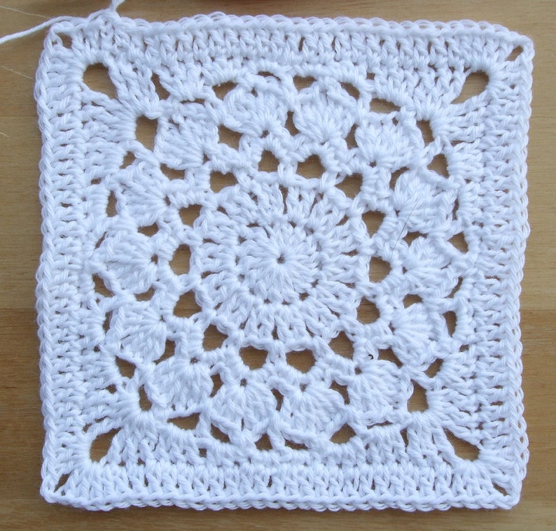 May include: White crochet square with a detailed, intricate pattern in the center. The square is made with a single crochet stitch and has a border around the edges.