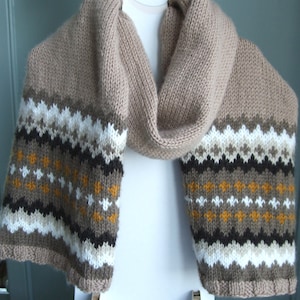 May include: A knitted scarf in shades of beige, brown, white, black, and mustard. The scarf has a geometric pattern on both ends, with a plain beige centre. The scarf is displayed against a white backdrop.