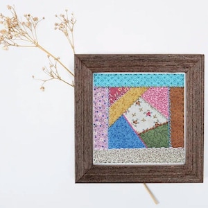 May include: A framed patchwork quilt square with a variety of colorful fabrics, including pink, blue, green, yellow, and brown. The quilt square is surrounded by a brown wooden frame.